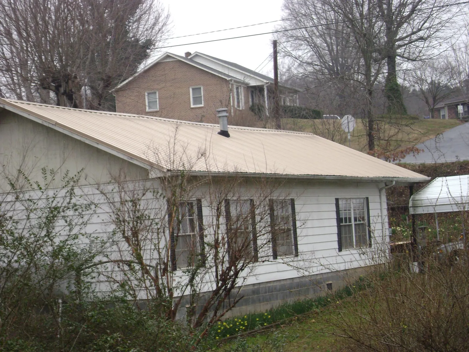 Tan metal roof on a white sided house set into a hillside — Commercial Roofing by Roofing Brothers in Oakland